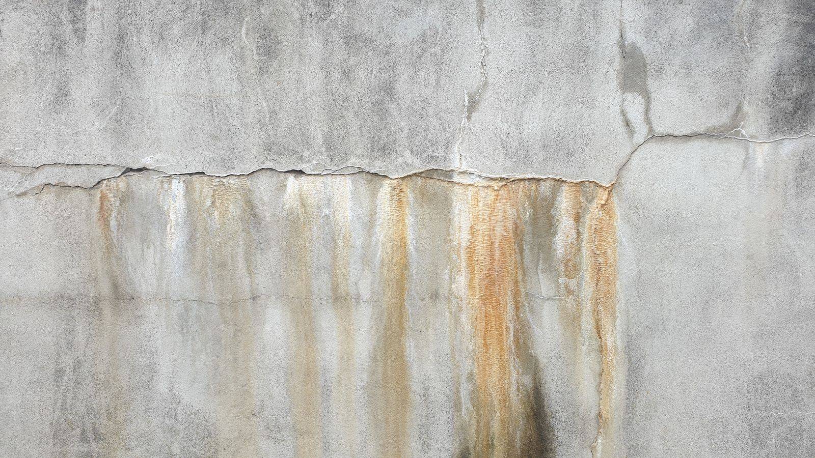 Concrete foundation wall with a long horizontal crack and rust-colored water stains streaking down from it, the classic sign of a leaking basement wall