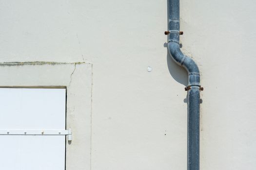 Close-up of a gray metal drainpipe attached to a plain exterior wall.